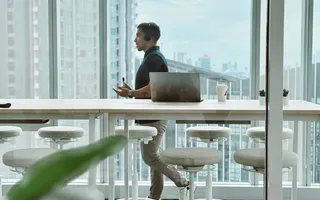 A specialist working on a laptop at a long table beside the Bangkok skyline