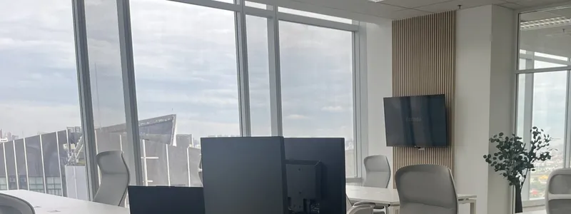 Desks and a wall-mounted screen at the Bangkok office, city skyline through the windows
