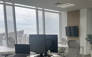 Desks and a wall-mounted screen at the Bangkok office, city skyline through the windows