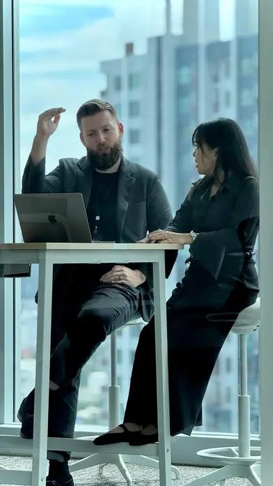Two members of our offshore development team talking at a laptop by a Bangkok office window