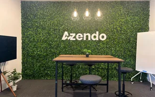 A standing meeting table in front of the green Azendo logo wall in Chiang Mai