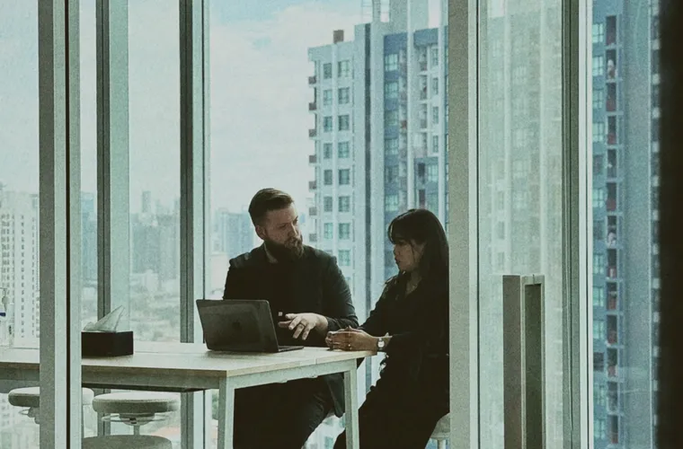 Two remote developers in a one-to-one review at a Bangkok office window