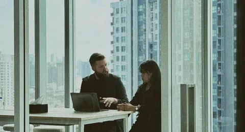 Two offshore developers in a one-to-one meeting by a Bangkok office window