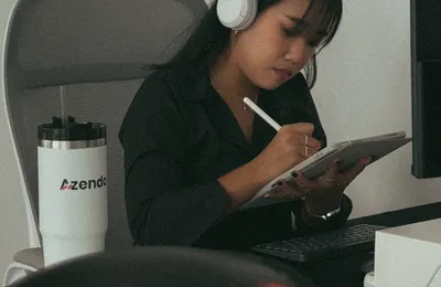A designer wearing headphones sketching on a tablet at her desk