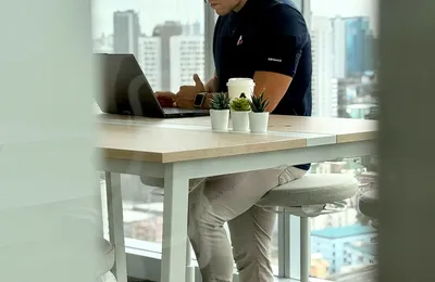 A specialist wearing headphones working on a laptop by the Bangkok office windows