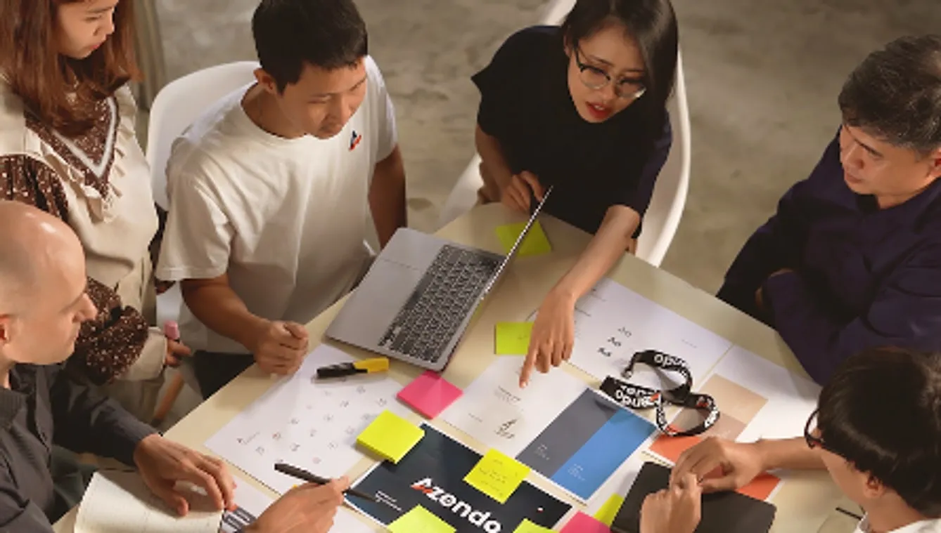 An Azendo team planning a sprint around a table with sticky notes and a laptop