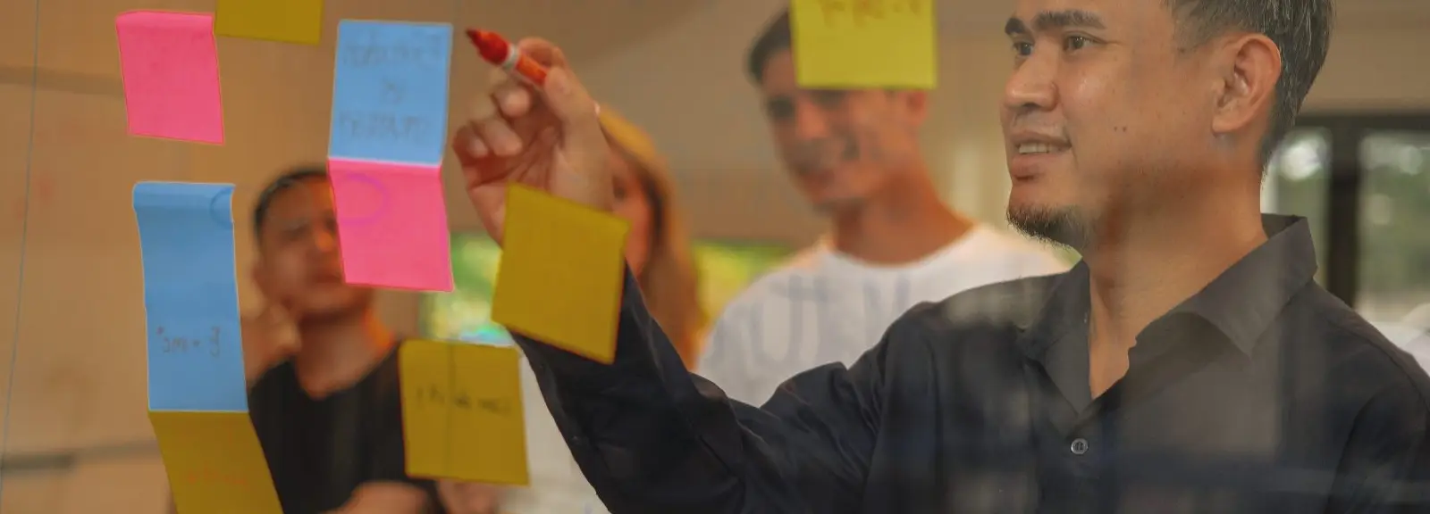 An Azendo specialist adding sticky notes to a glass wall during a workshop
