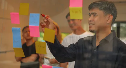 An Azendo specialist adding sticky notes to a glass wall during a workshop